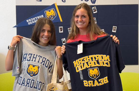 Two students holding t-shirts in the Graduate School office.